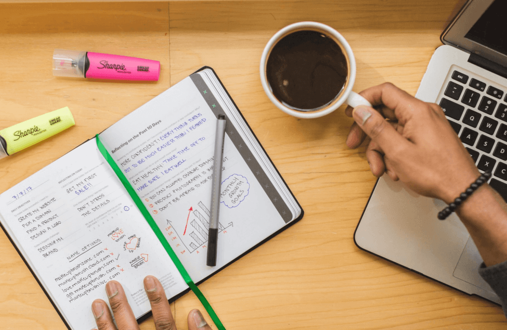 Person using notebook and holding a cup of coffee